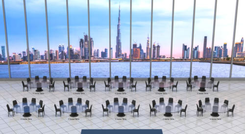 A modern conference room with round tables and chairs. The wall-length glass windows offer a panoramic view of the Dubai city skyline and water body. The horizon shows various skyscrapers against a twilight sky. Text labels indicate "5 Seater Table" on ea